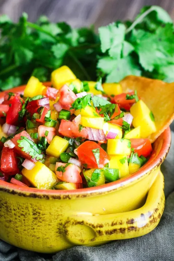 A-yellow-bowl-filled-with-mango-pico-de-gallo-with-cilantro-in-background.-taoofspice
